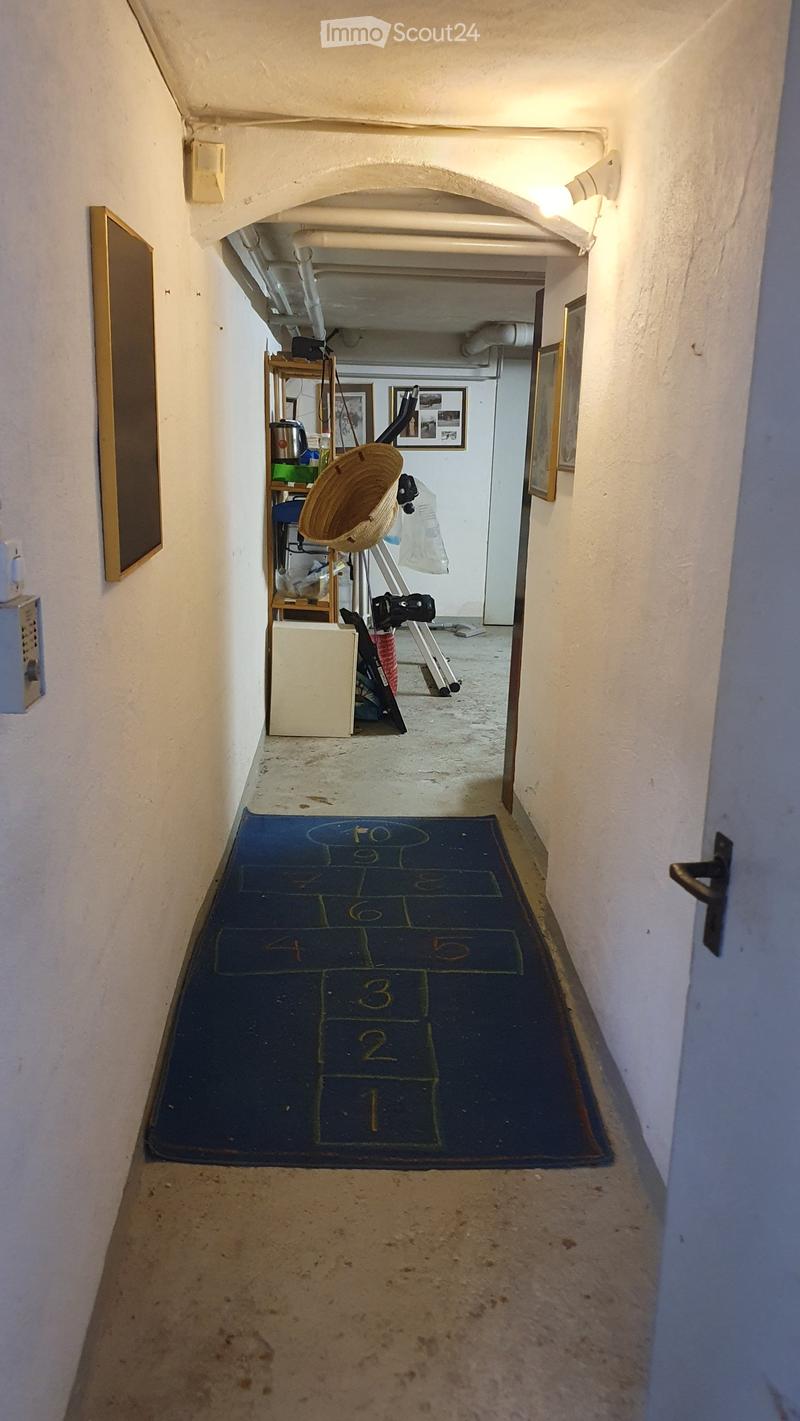 A narrow hallway with white walls, a blue numbered mat on the floor, and a small shelf with items in the background.