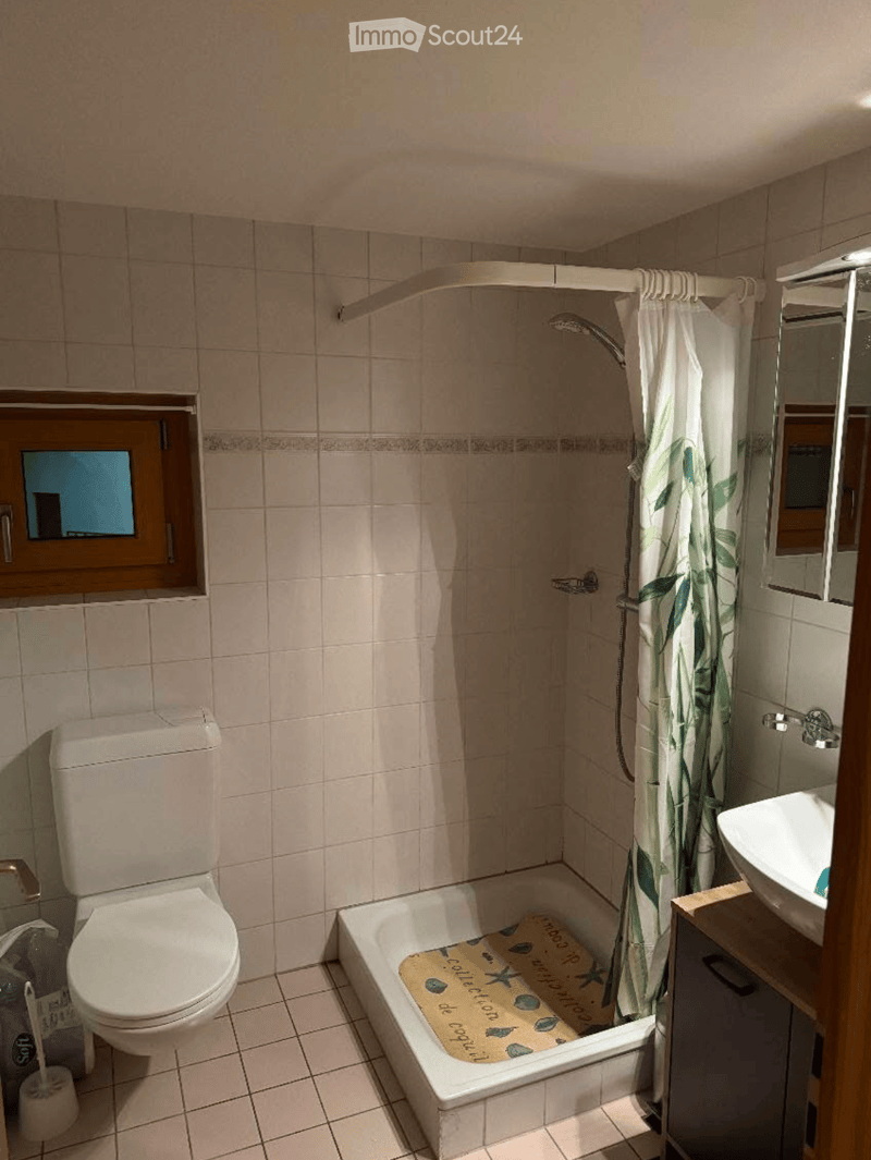 Bathroom with tiled walls and floor, featuring a toilet, bathtub with a decorative bath mat, a sink with a wooden cabinet, and a shower area with a curtain.