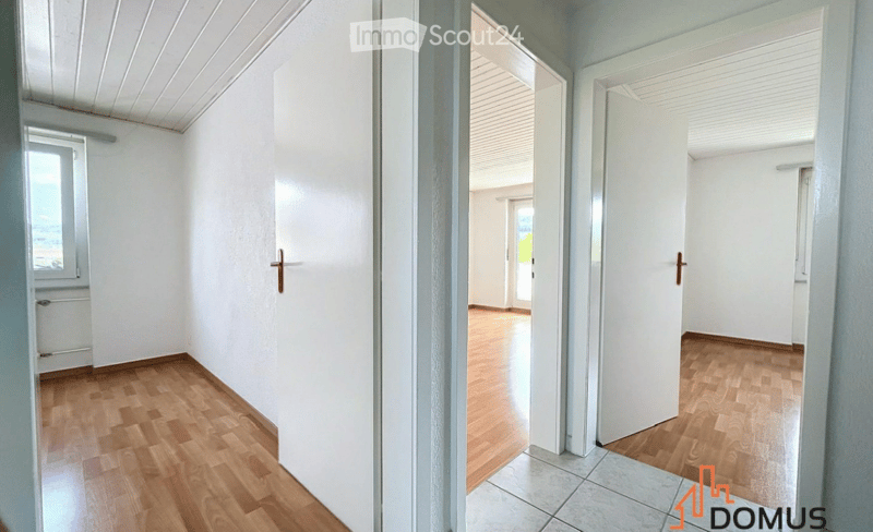 Empty hallway with wooden flooring, white walls, and multiple doors leading to other rooms.