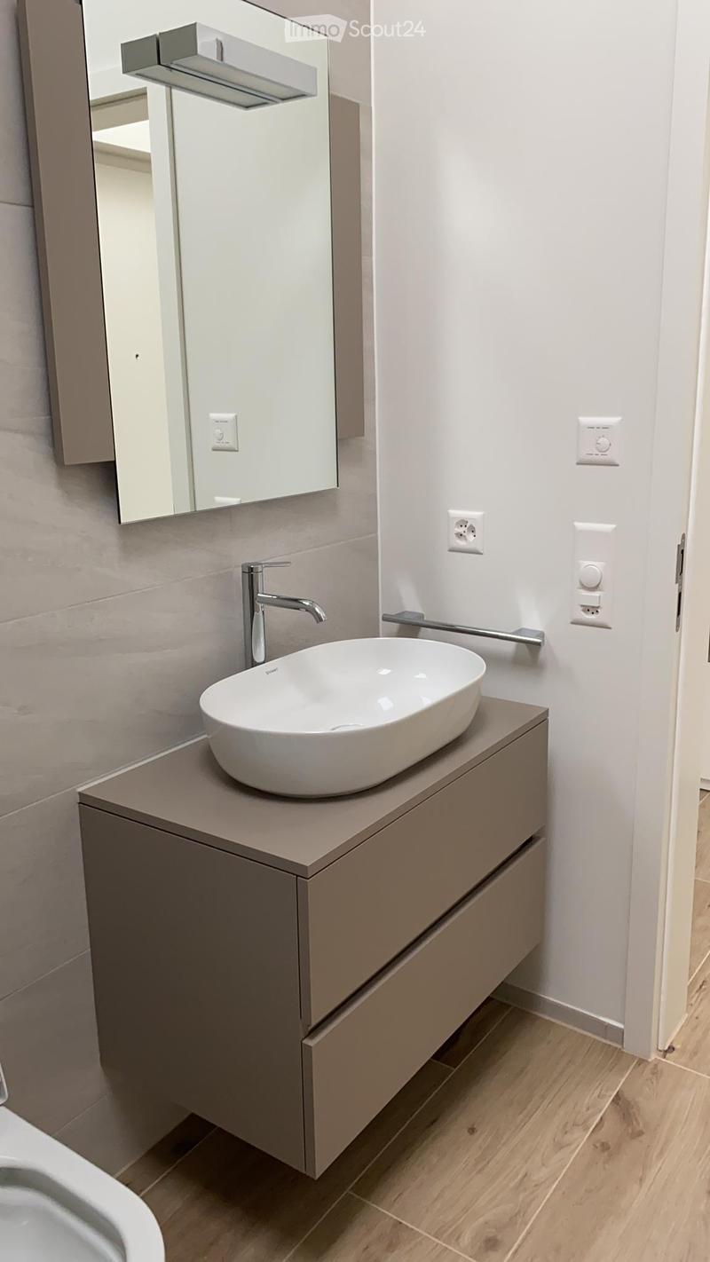 Modern bathroom with a sleek, minimalist design. Features a white sink with a modern faucet, a built-in cabinet, and a large mirror with integrated lighting.