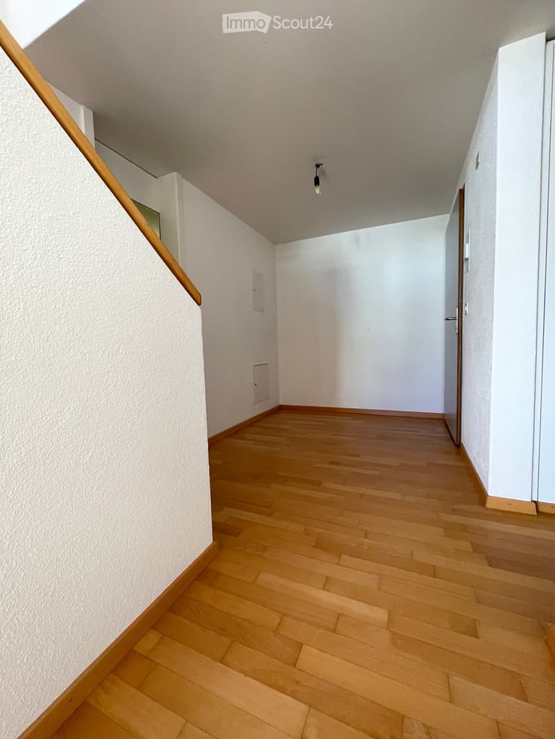 Staircase with wooden steps and handrail, white walls, and a closed door at the end.