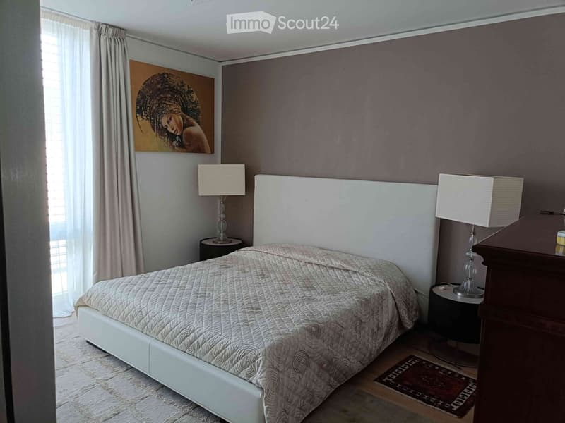 Modern bedroom with a large bed, white headboard, nightstands with lamps, and a painting on the wall.
