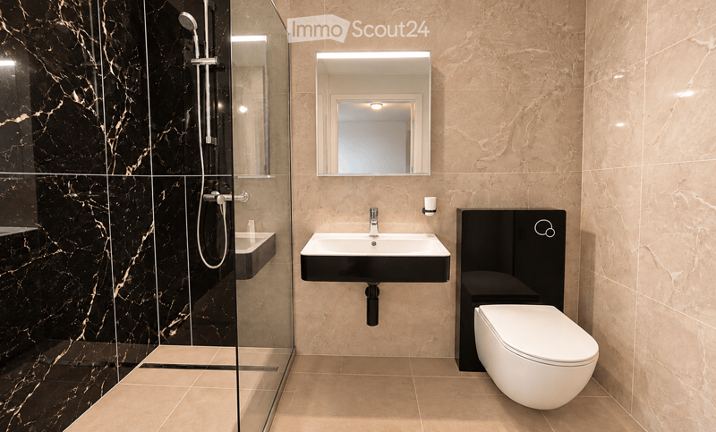 Modern bathroom with beige marble tiles, black accents, a glass-enclosed shower, a white toilet, and a black sink with a mirror above it.