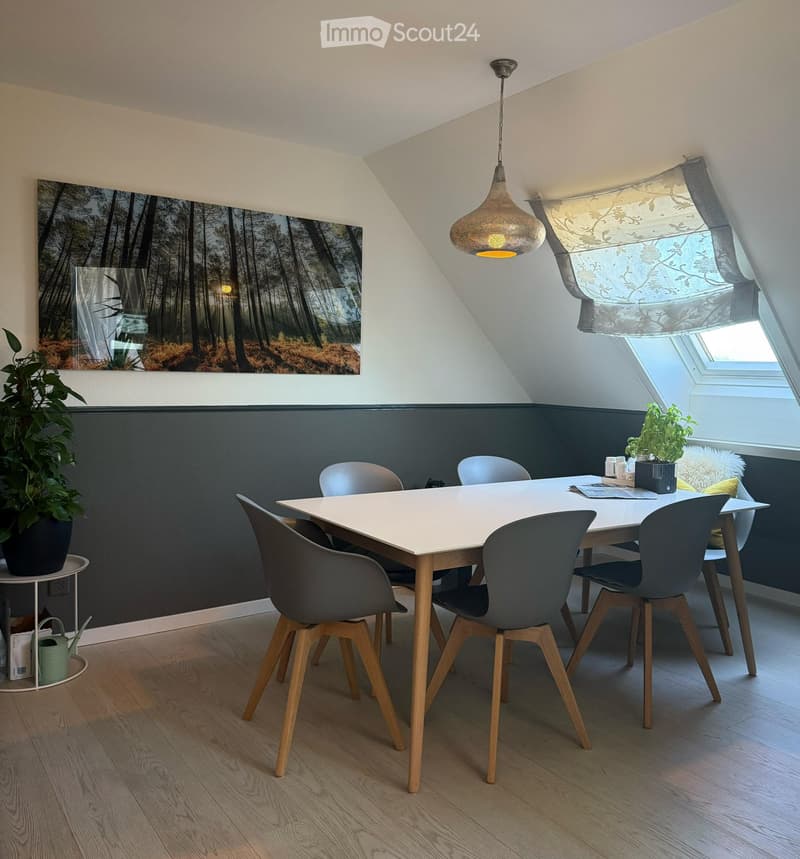 Modern dining area with a white dining table, six chairs, pendant light, and plants. Features a dark accent wall and large window with blinds.