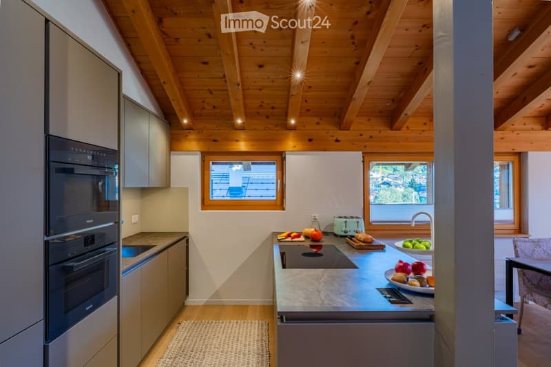 Modern kitchen with wooden ceiling beams, stainless steel appliances, granite countertops, and a variety of fresh fruits and vegetables on the counter.