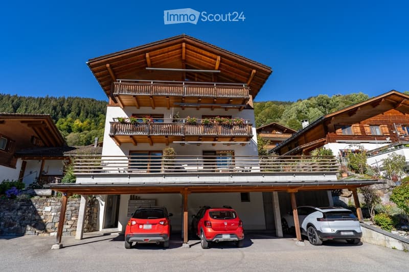 A two-story wooden house with balconies, a covered garage, and multiple parked cars.