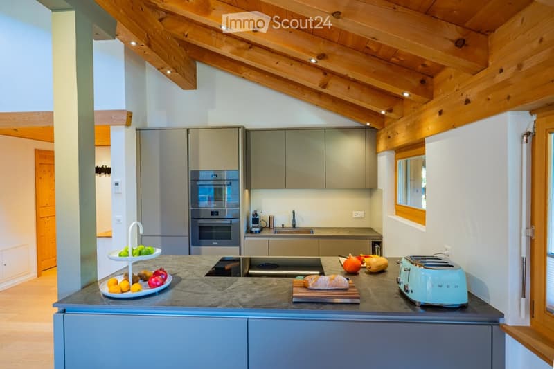 Modern kitchen with wooden beams, stainless steel appliances, and a marble countertop. Features include an oven, sink, toaster, and fresh fruits on the counter.