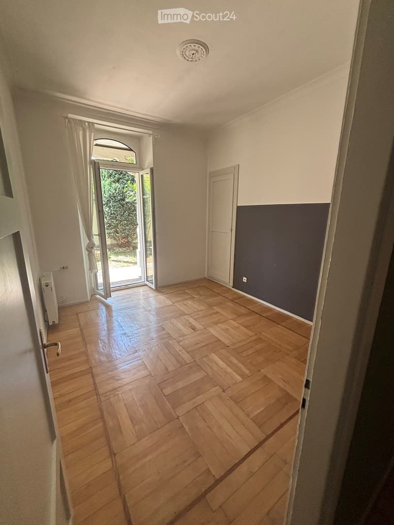 Empty room with wooden flooring, white walls, and a large sliding glass door leading to a garden area.