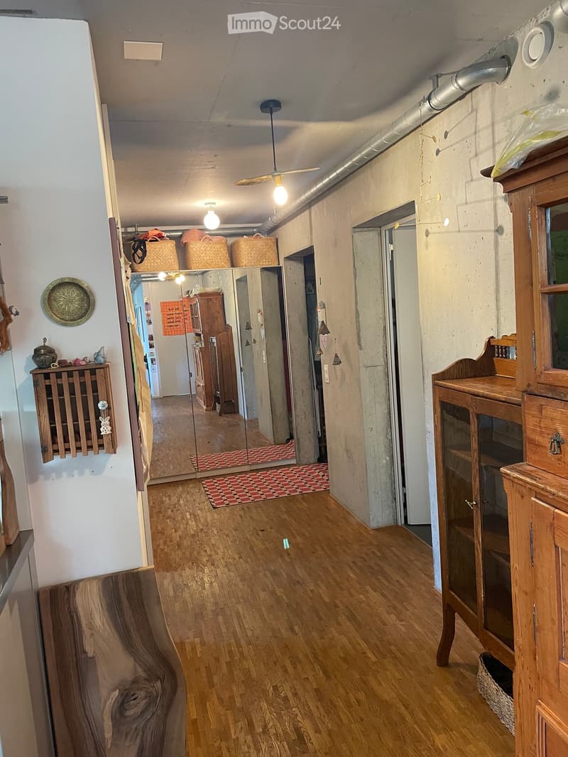 A long hallway with wooden flooring, a ceiling fan, and several doors leading to other rooms. There are wooden cabinets and a mirror on the walls.