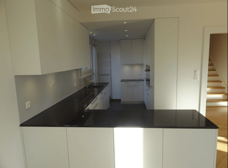 Modern kitchen with white cabinets, black countertop, built-in oven, and sink. The space is well-lit with recessed lighting and features a sleek, contemporary design.