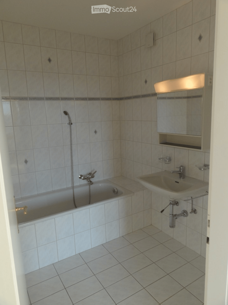Bathroom with tiled walls and floor, featuring a bathtub, sink, mirror, and light fixture.