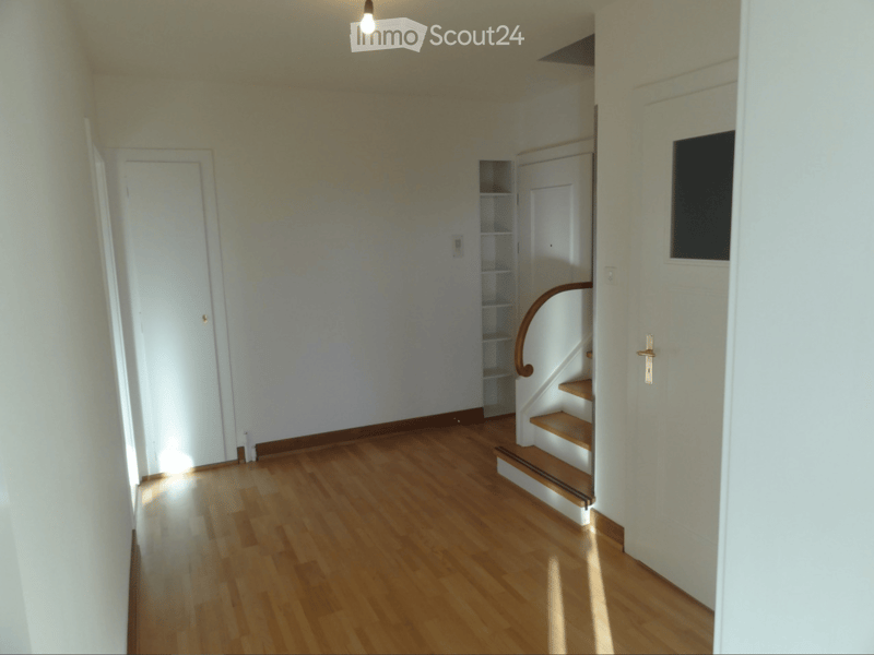 Empty hallway with wooden flooring, white walls, and a staircase leading upwards.