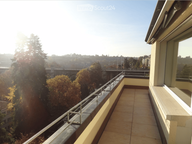 Balcony with tiled floor, metal railing, and scenic city view with trees and buildings.
