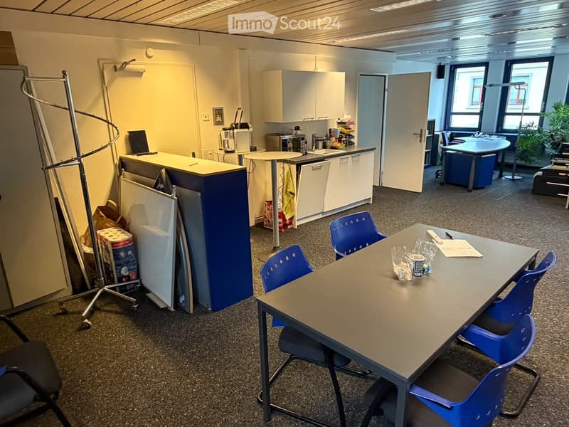 Office break room with a small kitchen area, a round table with chairs, a refrigerator, sink, and a plant near the window.
