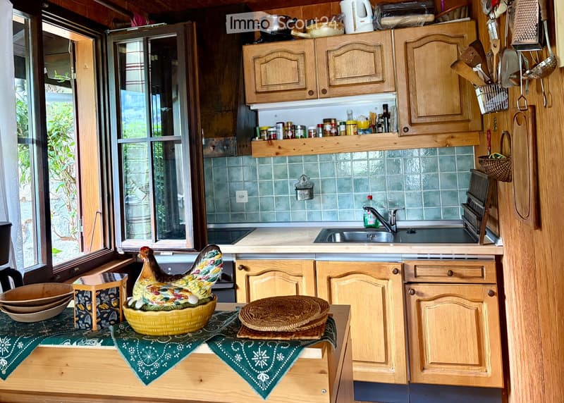 The kitchen features wooden cabinets, a sink with a faucet, and various kitchen utensils and appliances on the countertops. There is a decorative rooster figurine on a small table covered with a green cloth.