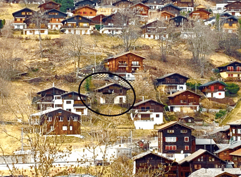 Aerial view of a village with multiple houses on a hillside, featuring wooden and stone structures with balconies and windows.