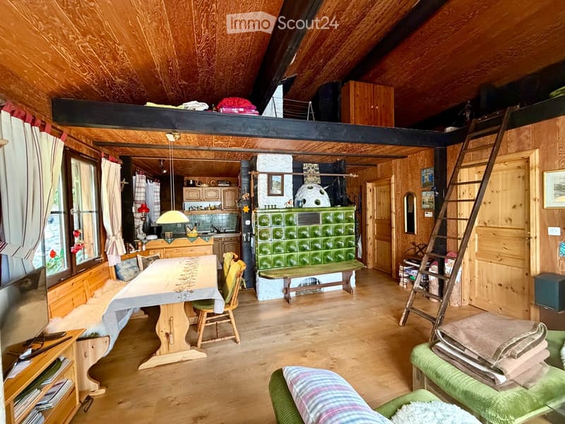 Cozy attic room with wooden walls and ceiling, featuring a dining area with a table and chairs, a green bench, a sofa, and a ladder leading to a loft area.