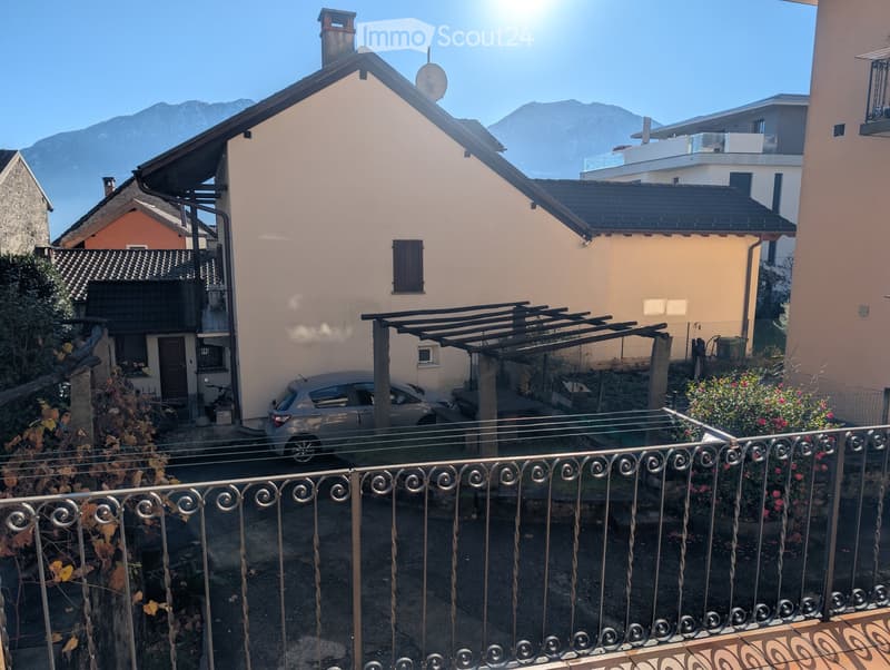 Balcony overlooking a residential area with houses, a parked car, and distant mountains under a clear blue sky.