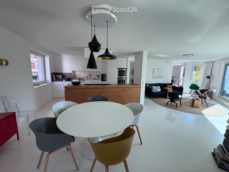 Modern open-plan living and dining area with a white dining table and chairs, a kitchen island, and a living room with a sofa and additional seating.