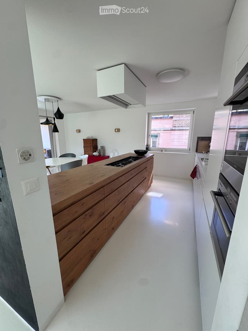 Modern kitchen with a wooden island, induction cooktop, built-in oven, microwave, and a small dining area with a table and chairs.