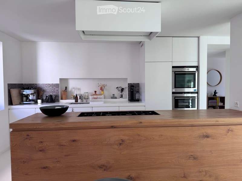 Modern kitchen with white cabinets, wooden island, stainless steel appliances, and various kitchen items on the counter.