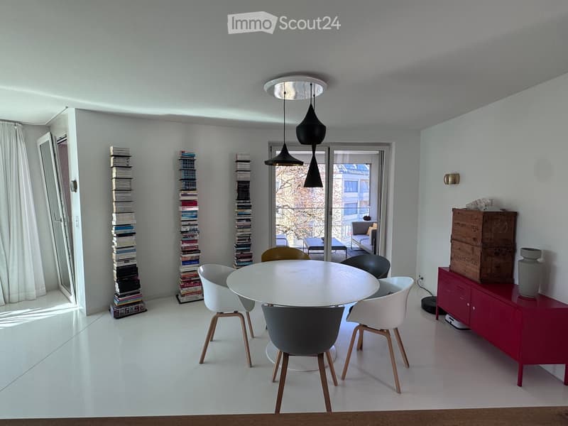 Modern dining area with white dining table, chairs, red cabinet, and decorative items.