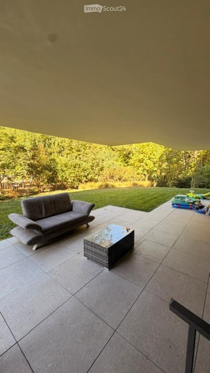Outdoor patio with a grey sofa, a coffee table, and a well-maintained lawn with trees in the background.