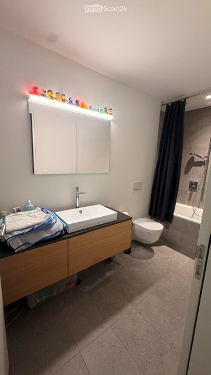 Modern bathroom with a white sink, mirror with LED lighting, toilet, bathtub, and dark curtains.