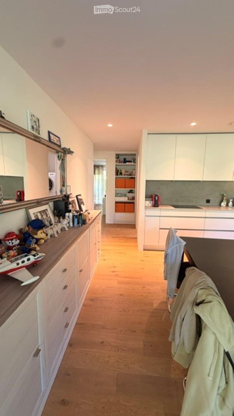 Bright, modern kitchen with white cabinets, wooden countertops, and a central island. The space features a light wooden floor, framed pictures on the wall, and various decorative items including toys and a model airplane on the counter.