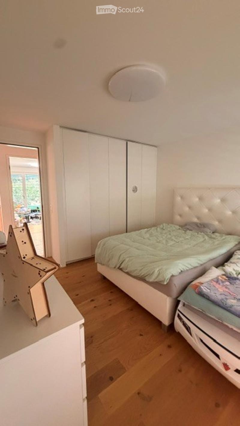 Bright bedroom with wooden flooring, white wardrobe, a bed with green bedding, a nightstand with a chair, and a mirror on the wall.