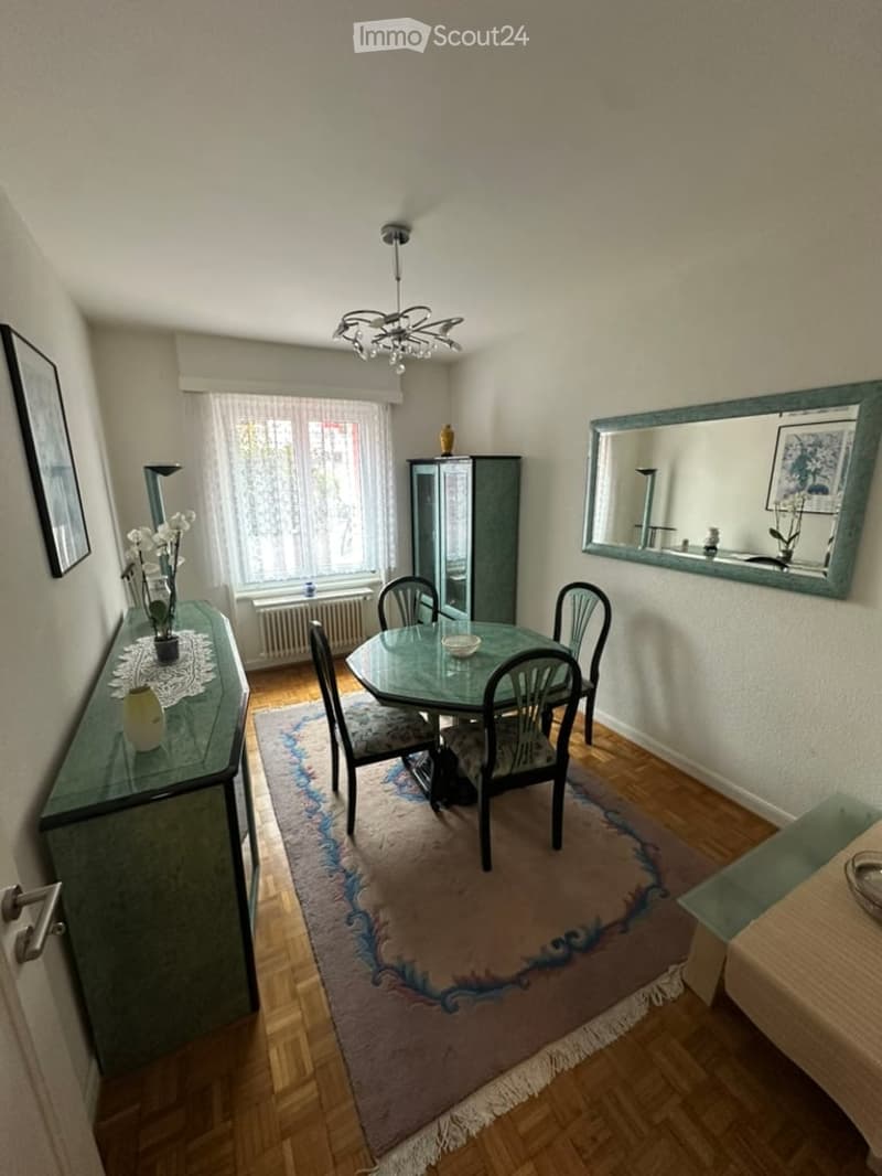Dining room with a round glass table, six chairs, a green sideboard, a large mirror, and a patterned rug.