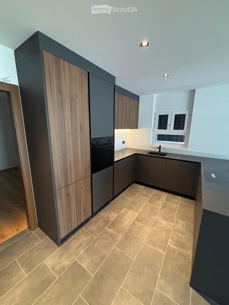 Modern kitchen with wooden and dark grey cabinets, tiled floor, and built-in appliances including an oven and sink.