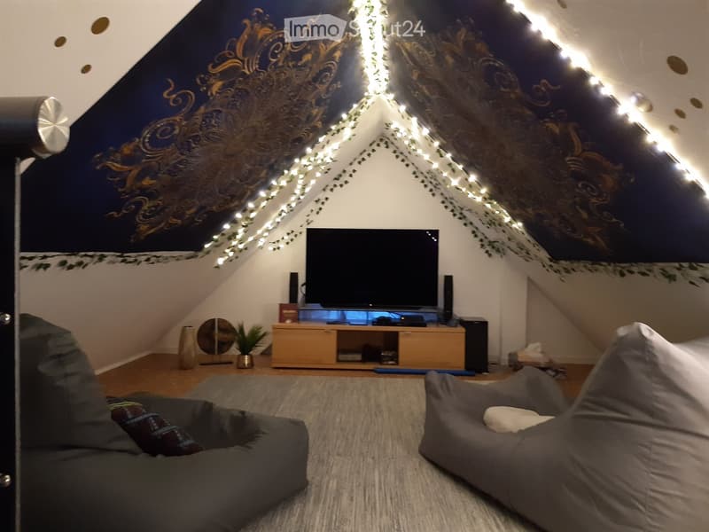 Cozy attic living space with slanted ceilings, string lights, a TV on a wooden stand, and two bean bag chairs on a rug.