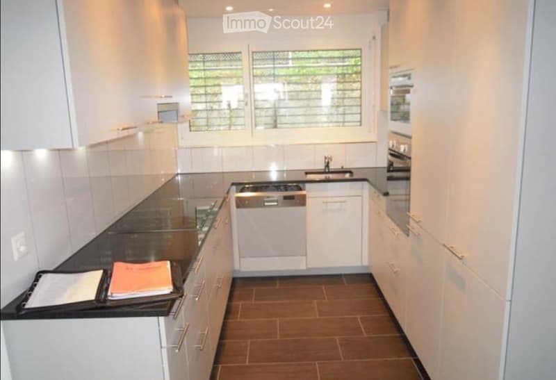 Modern kitchen with white cabinets, black countertop, stainless steel appliances, and a window with blinds.