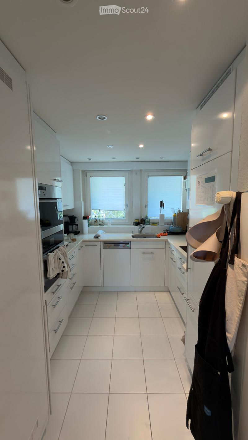 Modern kitchen with white cabinets, stainless steel appliances, and a central island. Features include a refrigerator, oven, dishwasher, and a sink with a window above it.