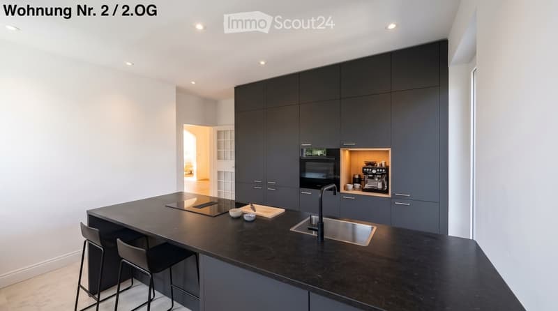 Modern kitchen with dark grey cabinets, black island, built-in appliances, and a sleek design.