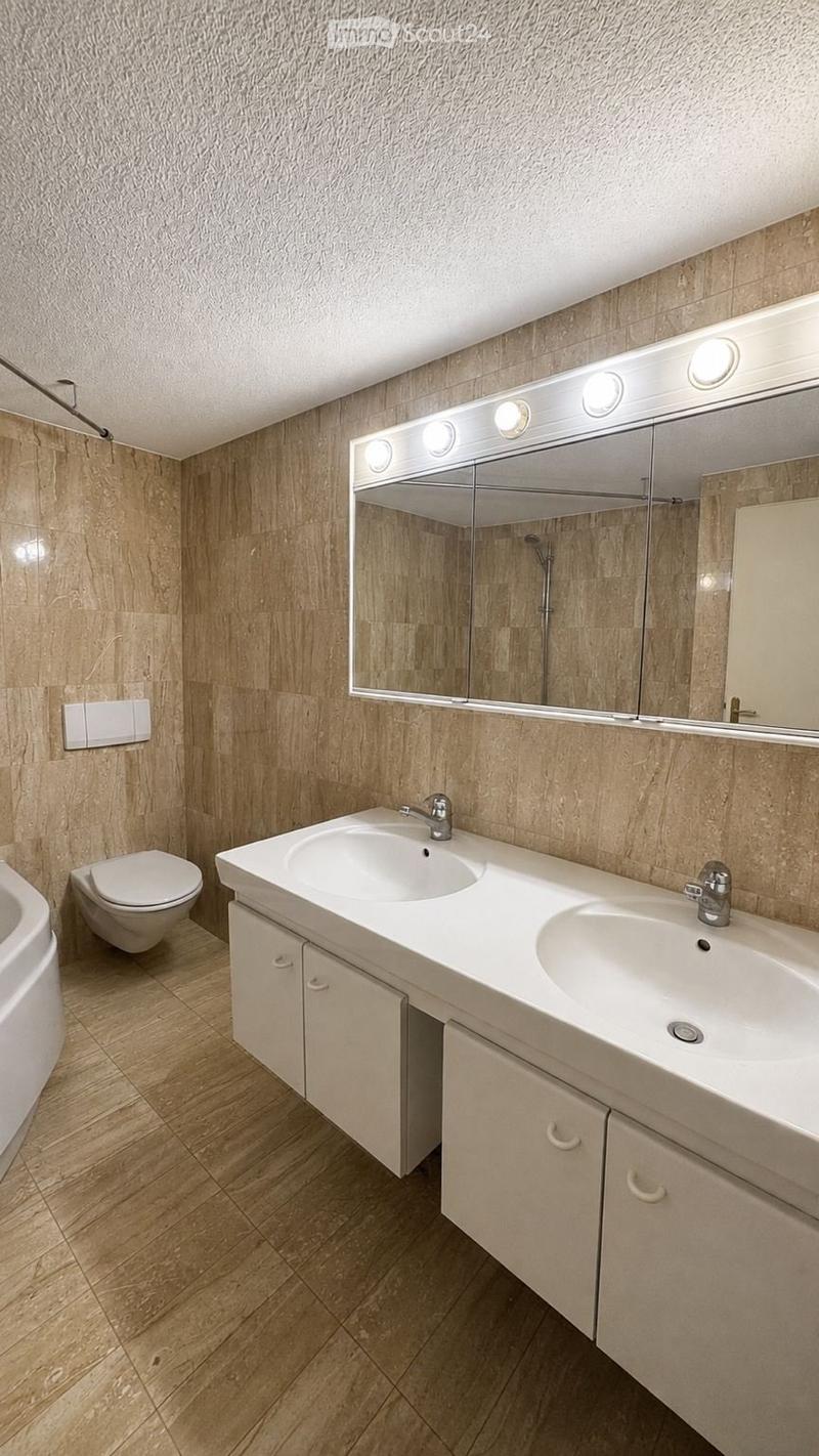 Modern bathroom with double sink vanity, large mirror with integrated lighting, toilet, bathtub, and wooden flooring.