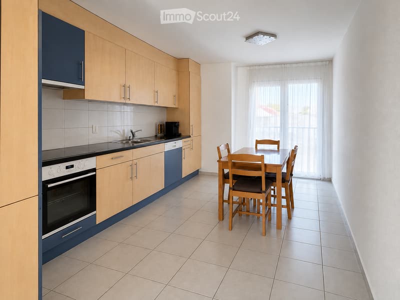 A modern kitchen and dining area with light wooden cabinets, stainless steel appliances, a sink, and a dining table with chairs.