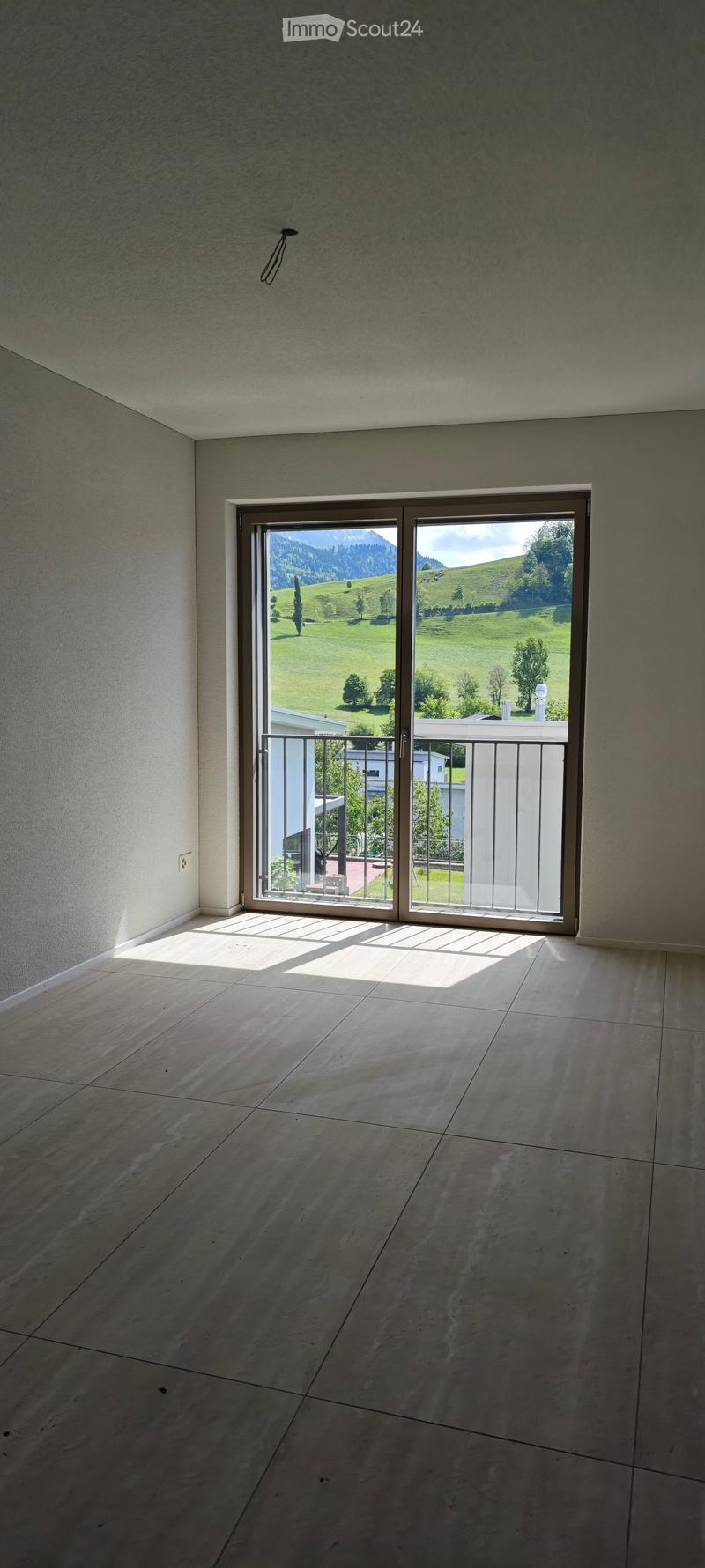 Empty room with large sliding glass doors leading to a balcony, tiled floor, and natural light from the view of green hills and mountains.