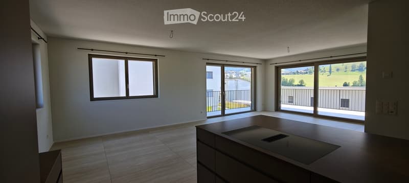 Empty room with large windows and sliding doors leading to a balcony, featuring a modern kitchen island and tiled floor.