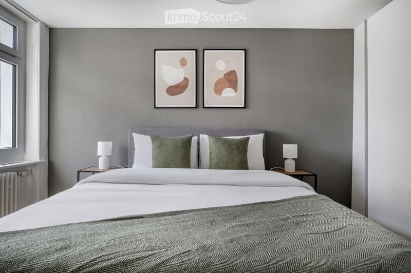 Modern bedroom with a large bed, white linens, green pillows, two nightstands with lamps, and two abstract picture frames on the wall.