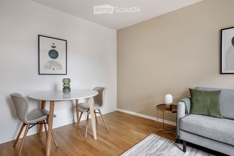 Modern living room with a grey sofa, coffee table, side table, dining table, chairs, and decorative items.