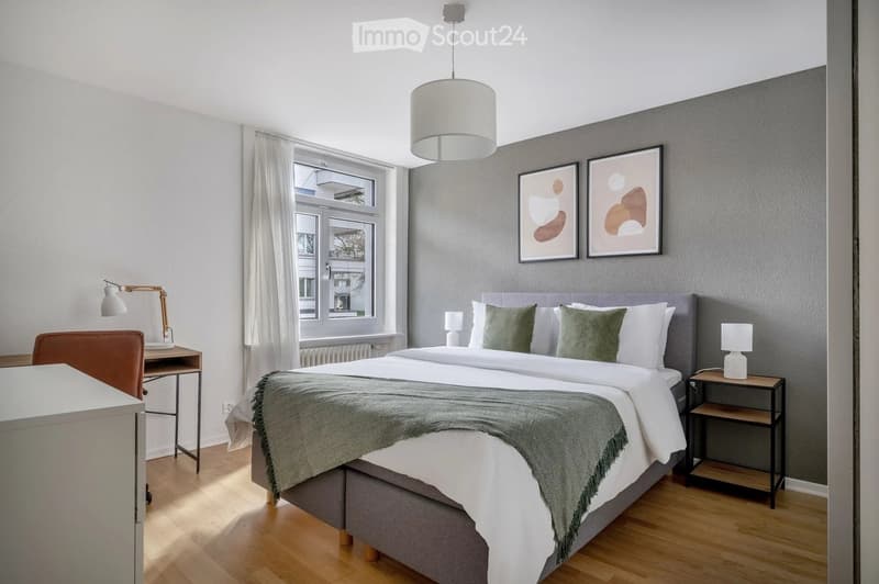 Modern bedroom with a large bed, nightstands, desk, and artwork on the wall.