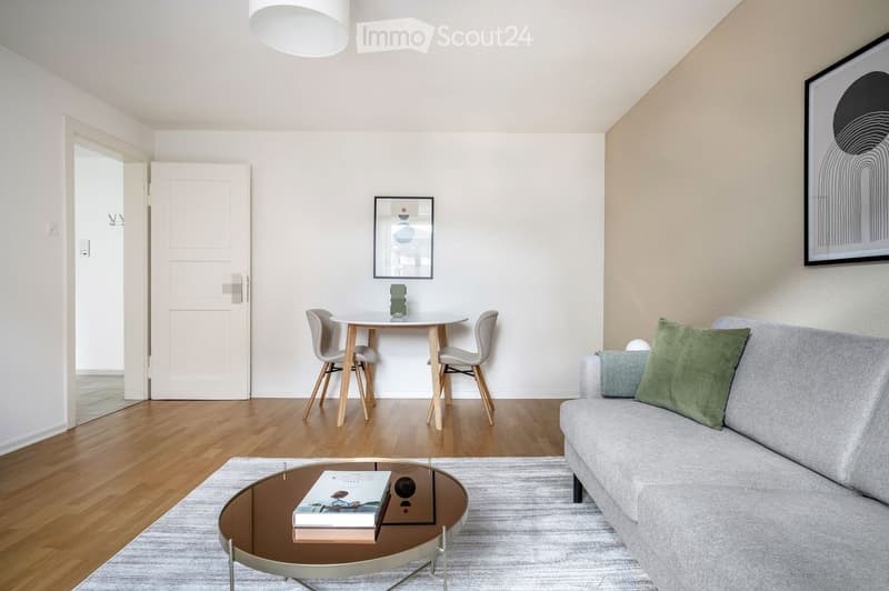 Modern living and dining area with a grey sofa, coffee table, dining table with chairs, and artwork on the walls.