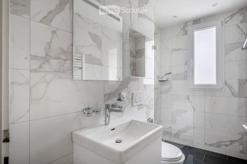 Modern bathroom with marble tiles, a white sink, a mirror, a shower, and a toilet.