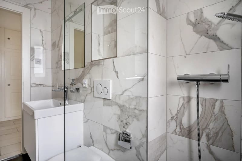 Modern bathroom with marble tiles, a white sink, a glass-enclosed shower area, and a toilet.