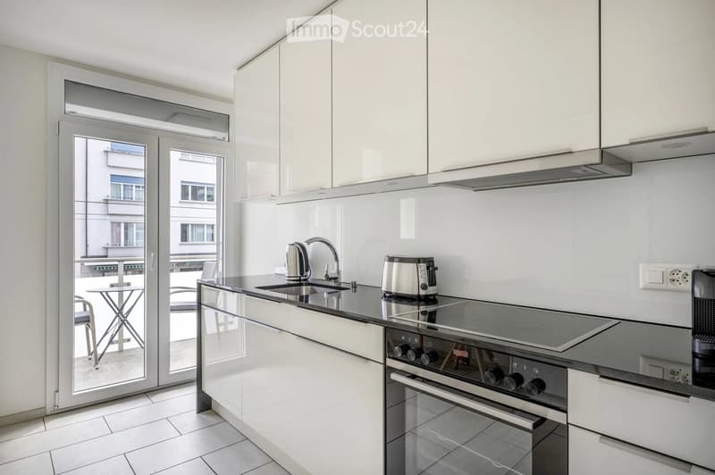 Modern kitchen with white cabinets, stainless steel appliances, and a large window offering a view of the city.