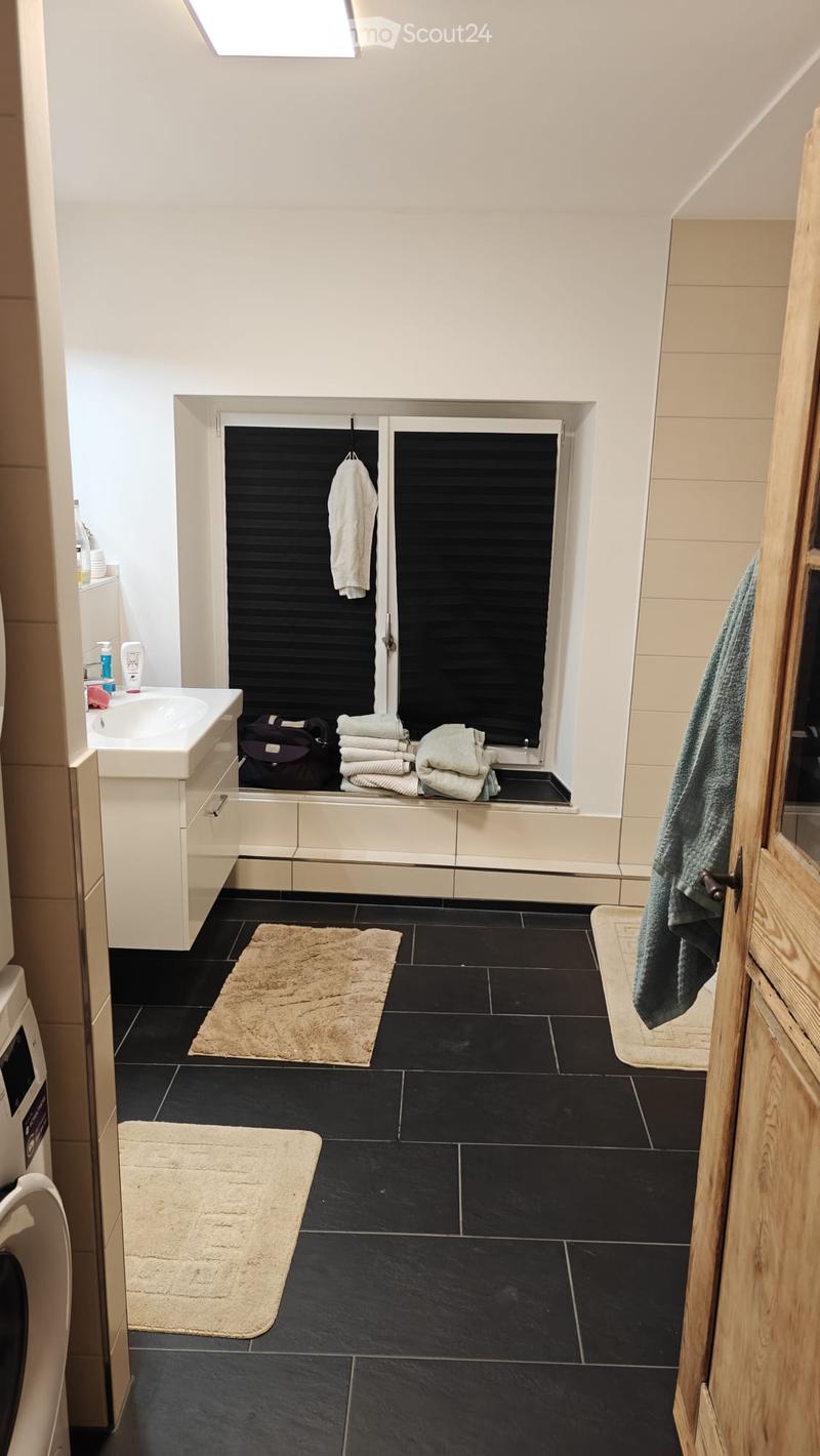 Modern bathroom with black tiled floor, white walls, a sink with a cabinet, a mirror, towels, and a small window with blinds.