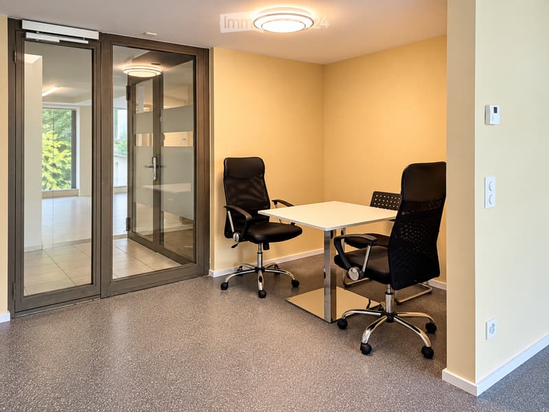 A small, furnished room with a white table and two black office chairs, carpeted floor, and large glass doors leading to an outdoor area.