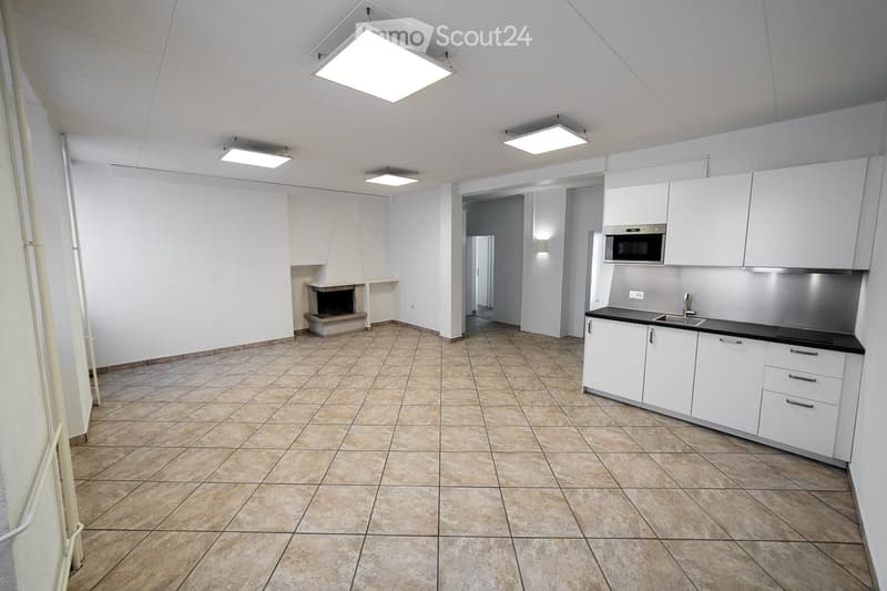 Empty kitchen and living area with white cabinets, stainless steel appliances, tiled floor, and a fireplace.